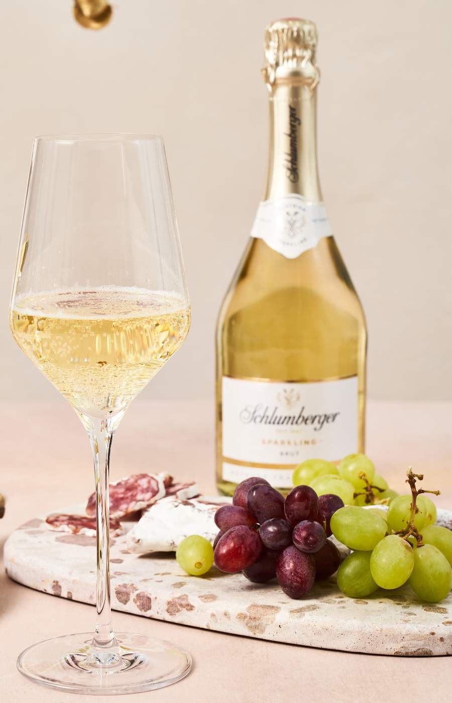 Eine geöffnete Schlumberger Sparkling Flasche steht auf einem Tisch mit gefülltem Glas und Käseplatte