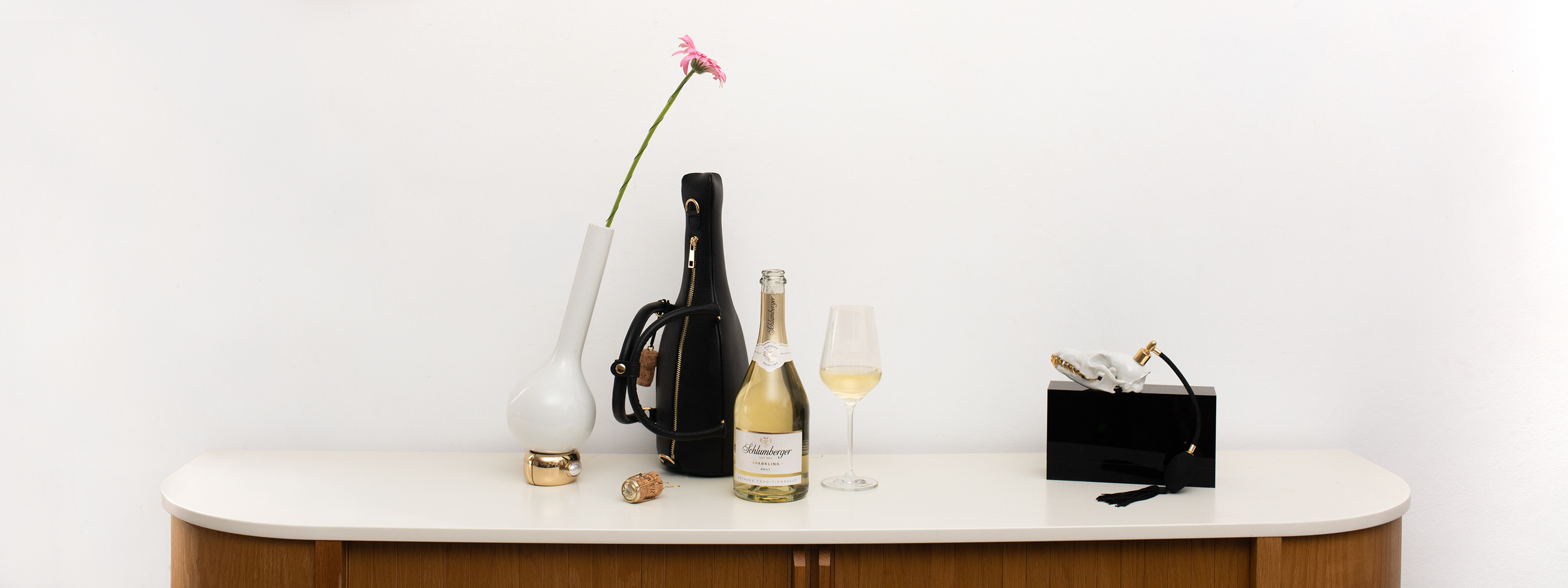 Schwarze Tasche steht auf Kommode mit einer Flasch sparkling einem Glas und einer Blume