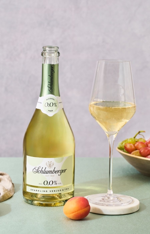 Sparkling Verjus & Tea Flasche steht mit Ewinglas und Marille am Tisch
